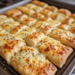 "Homemade cheesy breadsticks baked golden brown, topped with melted mozzarella and parmesan, served with marinara sauce."