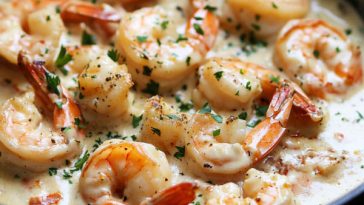 “A skillet filled with creamy garlic shrimp garnished with parsley, served with pasta and lemon wedges.”