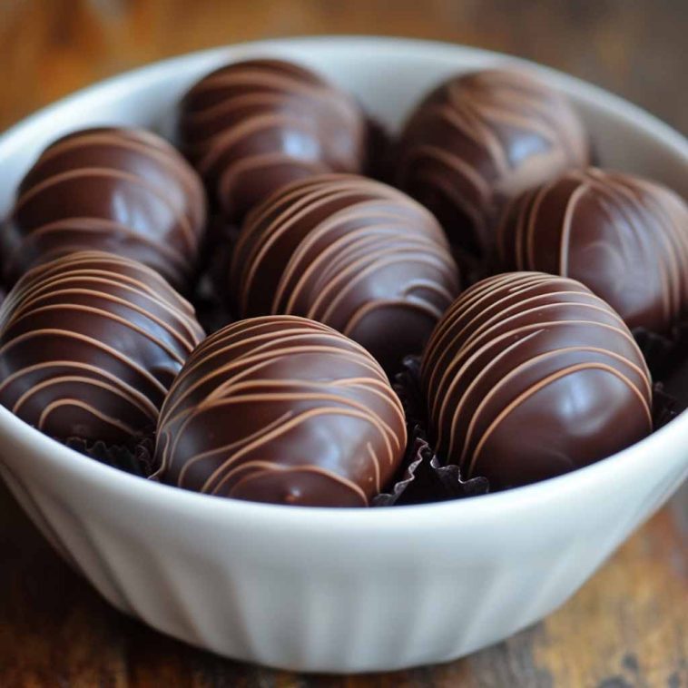 A white bowl filled with round, dark chocolate truffles decorated with fine milk chocolate drizzles, arranged neatly on a wooden surface.
