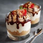 A glass jar filled with whipped cottage cheese peanut butter mousse, topped with crushed peanuts and a drizzle of honey, served with a spoon.