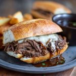 Slow-cooked French dip sandwiches with tender shredded beef piled on toasted hoagie rolls, served with a bowl of rich au jus for dipping.
