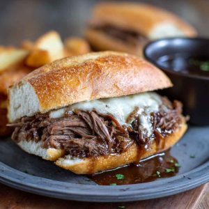 Slow-cooked French dip sandwiches with tender shredded beef piled on toasted hoagie rolls, served with a bowl of rich au jus for dipping.