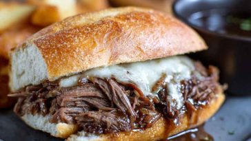 Slow-cooked French dip sandwiches with tender shredded beef piled on toasted hoagie rolls, served with a bowl of rich au jus for dipping.