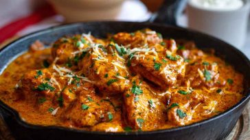 Golden skillet of butter chicken with creamy sauce, garnished with herbs and served with mashed potatoes.