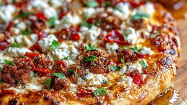 A golden pizza topped with spicy sausage, crumbled feta, and a drizzle of honey, served on a rustic board with chili flakes and fresh herbs.