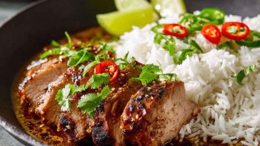 Zesty ginger lime pork slices served over creamy coconut rice, garnished with fresh cilantro, lime wedges, and chili flakes on a ceramic plate.