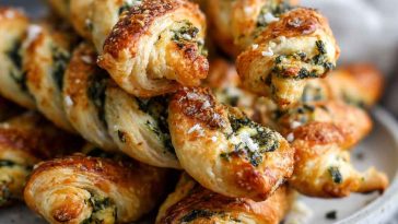 Golden spinach and feta puff pastry twists with flaky layers, filled with creamy feta and sautéed spinach, served on a rustic wooden board.