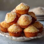 Golden Portuguese coconut cakes with a moist, fluffy texture, topped with shredded coconut and lightly caramelized edges, served on a vintage dessert plate.