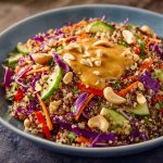 Crunchy Thai quinoa salad with colorful vegetables, fresh herbs, and creamy peanut dressing, served in a bowl and garnished with chopped peanuts and lime wedges.