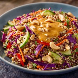Crunchy Thai quinoa salad with colorful vegetables, fresh herbs, and creamy peanut dressing, served in a bowl and garnished with chopped peanuts and lime wedges.