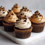 A decadent chocolate cupcake topped with creamy coffee frosting and chocolate shavings, served on a rustic plate with a cup of espresso.