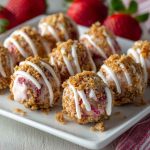 Mini strawberry cheesecake crunch bites topped with crushed golden cookies, fresh strawberry slices, and creamy cheesecake filling, served on a dessert platter.