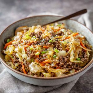 A skillet filled with browned ground beef, tender cabbage, and carrots tossed in a savory garlic-ginger stir fry sauce, garnished with scallions.