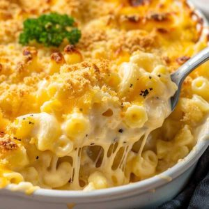 A bowl of creamy macaroni and cheese with golden cheddar sauce coating elbow pasta, garnished with parsley and served warm.