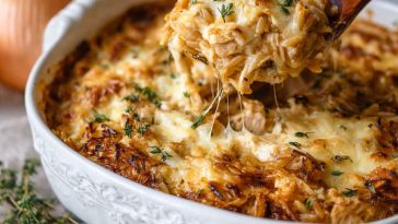 A golden-baked French onion chicken orzo casserole in a skillet, topped with melted cheese, caramelized onions, and fresh thyme sprigs.