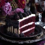 A rich blackberry velvet gothic cake with deep purple layers, glossy blackberry glaze, and dark floral accents on a moody cake stand.
