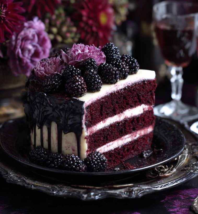 A rich blackberry velvet gothic cake with deep purple layers, glossy blackberry glaze, and dark floral accents on a moody cake stand.