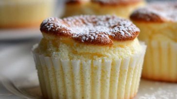 Mini Japanese cotton cheesecake cupcakes with golden tops, dusted with powdered sugar and served in white cupcake liners.