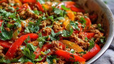 Ground turkey sautéed with red, yellow, and green bell peppers in a skillet, garnished with herbs.