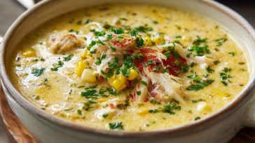 A creamy bowl of crab and corn chowder garnished with fresh herbs, featuring chunks of sweet corn, tender crab meat, and smoky bacon in a rich broth.
