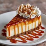 A rich caramel apple cheesecake topped with cinnamon-spiced apple slices and a glossy caramel drizzle, served on a rustic dessert plate.