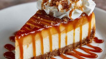 A rich caramel apple cheesecake topped with cinnamon-spiced apple slices and a glossy caramel drizzle, served on a rustic dessert plate.