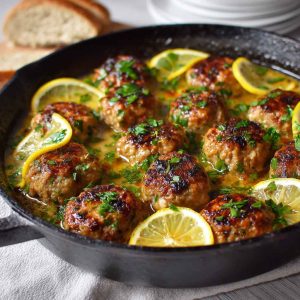 Tender Greek meatballs served in a creamy lemon sauce, garnished with fresh dill and lemon zest on a white plate.