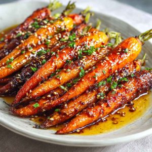 Golden roasted carrots glazed with honey and garlic, garnished with fresh herbs on a rustic serving tray.