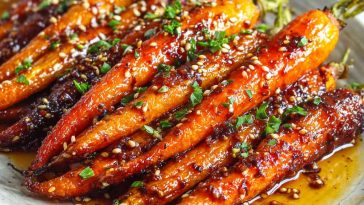Golden roasted carrots glazed with honey and garlic, garnished with fresh herbs on a rustic serving tray.