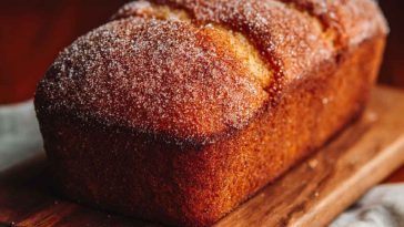 Golden spiced apple cider donut loaf dusted with cinnamon sugar, sliced and served with fresh apple slices and warm cider.