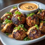 Glazed Korean BBQ meatballs served with a side of spicy mayo dip and garnished with sesame seeds and scallions.