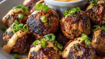 Glazed Korean BBQ meatballs served with a side of spicy mayo dip and garnished with sesame seeds and scallions.