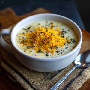 Creamy cheddar garlic herb potato soup in a bowl, garnished with fresh herbs and shredded cheese.