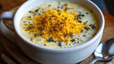 Creamy cheddar garlic herb potato soup in a bowl, garnished with fresh herbs and shredded cheese.