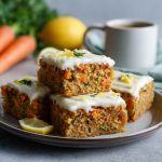 Light carrot and zucchini bars topped with creamy lemon frosting, served in squares with visible shreds of carrot and zucchini, garnished with lemon zest.