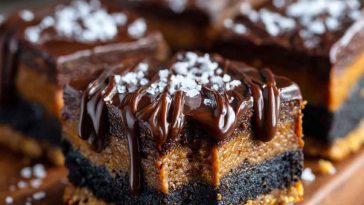 A tray of chocolate cheesecake bars with a chocolate cookie crust, creamy cheesecake layer, and glossy chocolate ganache topping, cut into perfect squares.