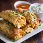 Crispy golden egg rolls filled with creamy buffalo chicken dip, served with ranch dressing and garnished with chopped green onions.