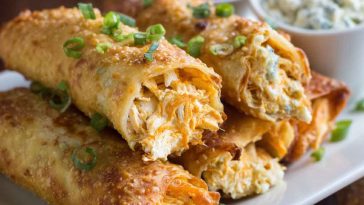 Crispy golden egg rolls filled with creamy buffalo chicken dip, served with ranch dressing and garnished with chopped green onions.