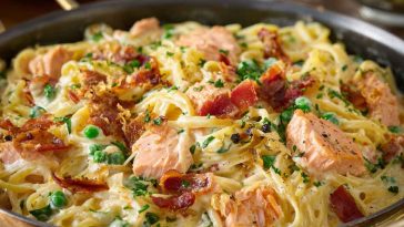 A plate of smoked salmon carbonara with creamy pasta ribbons, flecks of pink salmon, cracked black pepper, and fresh herbs, served with lemon wedges.