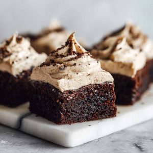 Frosted coffee brownies stacked on a plate with creamy coffee frosting and chocolate shavings on top.