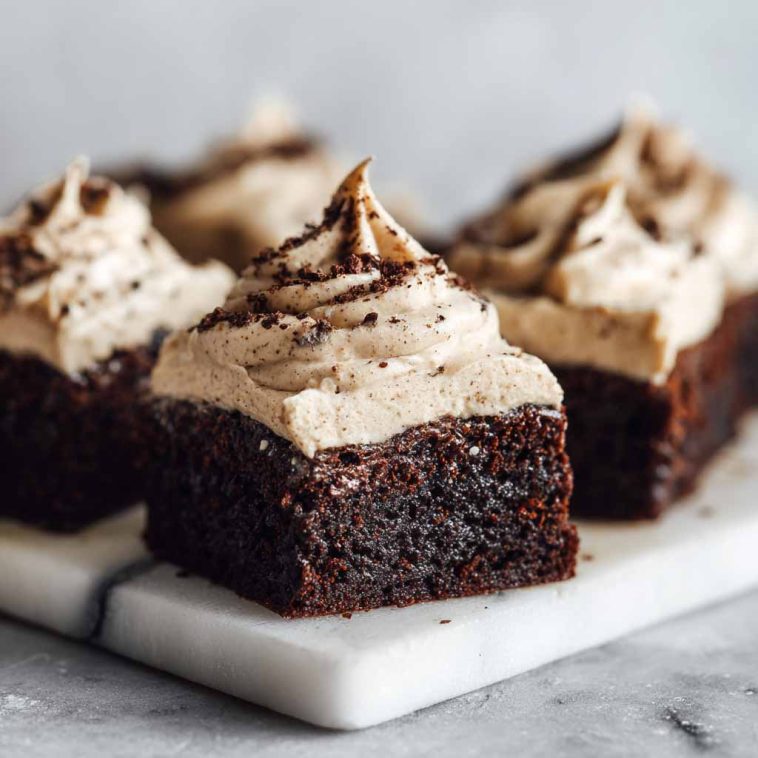 Frosted coffee brownies stacked on a plate with creamy coffee frosting and chocolate shavings on top.