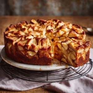 A golden slice of apple pie cake with tender apple layers, cinnamon crumble topping, and a moist cake base served on a cozy ceramic plate.