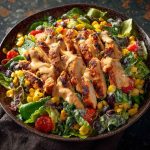 A colorful bowl of Southwest chicken salad with grilled chicken, black beans, corn, avocado, cherry tomatoes, and a creamy chipotle dressing.