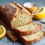 Luscious lemon zucchini bread with a golden crust, moist interior, and lemon glaze drizzle, garnished with lemon zest and served in thick slices.