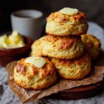 Golden keto biscuits stacked on a plate with melted butter and fresh herbs.
