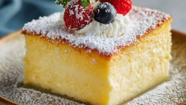 A slice of vanilla magic custard cake showing its three distinct layers—fluffy sponge, creamy custard, and dense base—garnished with powdered sugar.