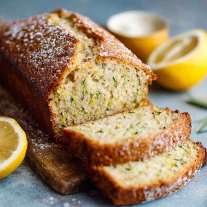 Luscious lemon zucchini bread with a golden crust, moist interior, and lemon glaze drizzle, garnished with lemon zest and served in thick slices.