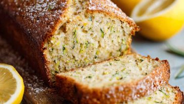Luscious lemon zucchini bread with a golden crust, moist interior, and lemon glaze drizzle, garnished with lemon zest and served in thick slices.