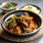 Slow-cooked Moroccan lamb tagine served in a traditional clay dish, garnished with dried apricots, almonds, and fresh herbs.