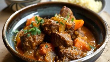 Slow-cooked Moroccan lamb tagine served in a traditional clay dish, garnished with dried apricots, almonds, and fresh herbs.
